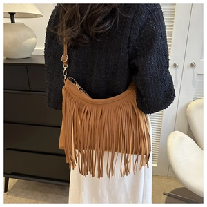 Brown faux leather shoulder bag with long tassels shown on model in a modern home interior