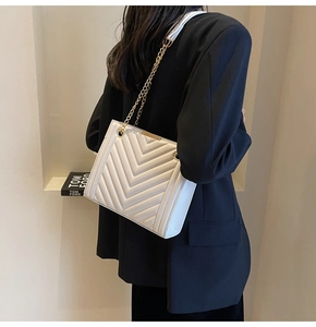 Modern white crossbody bag with V-shaped quilting and elegant gold chain strap on model