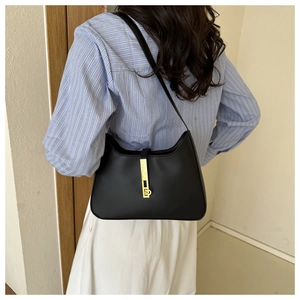 Detail of a black leather hobo bag with gold hardware worn by a model in a casual setting