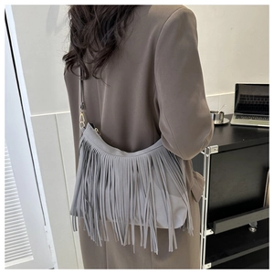 Detail of grey fringe crossbody bucket bag with suede texture and metallic buckles