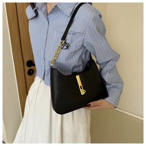 Détail du sac sous l'aisselle en cuir noir avec fermoir doré et bandoulière en chaîne