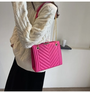Detail view of a magenta crossbody bag with V-shaped quilted pattern and gold chain strap