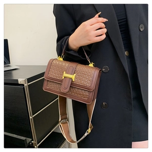 Détail d'un sac à main marron à texture tissée avec un fermoir en métal doré brillant
