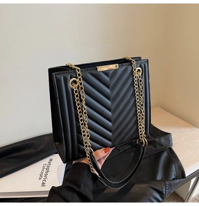 Detail of black quilted shoulder bag with V-shaped stitching and gold chain strap