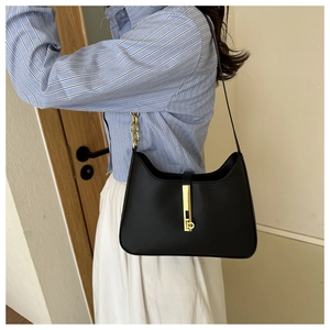 Detail of a chic black PU leather underarm bag with gold metal buckle on a shoulder model