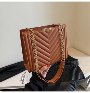 Detail of brown quilted faux leather bag with V-shaped stitching and golden chain strap