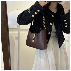 Detail of dark brown leather crossbody bag with gold metal buckle and chain strap on model