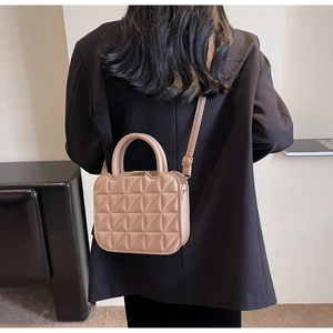 Dettaglio della borsa a tracolla trapuntata beige con motivi geometrici e fibbie dorate