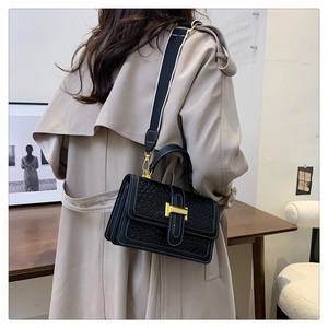 Detail of black woven crossbody bag with white stitching and gold H-buckle on a trench coat