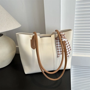 Chic beige tote bag with brown handles and checkered scarf on a black desk