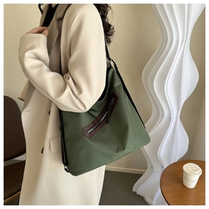 Detail of army green nylon tote bag featuring front diagonal zipper and leather trim