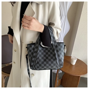 Close-up of stylish black and gray checkered tote bag styled with a beige coat