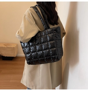 Detail of black quilted puffer tote bag with square stitching worn over a beige coat