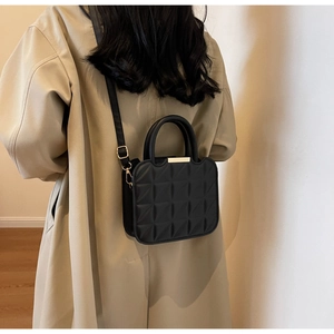 Dettaglio borsa trapuntata nera con chiusura dorata su trench beige elegante