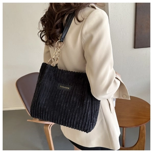Detail of black corduroy tote bag with gold chain strap and FASHION label on beige blazer