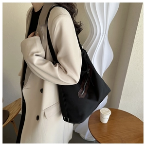 Detail view of a large black tote bag with brown leather trim zipper on a female model