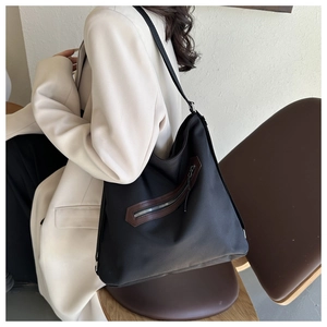 Detail of black canvas tote bag with brown leather zipper trim and long shoulder strap