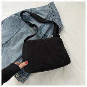 Detail view of black corduroy messenger bag featuring adjustable canvas strap and vertical texture
