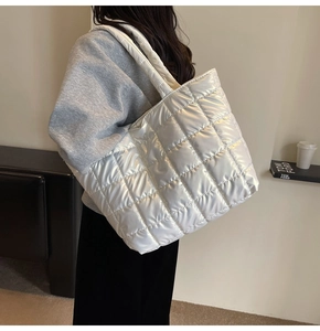 Detail of a large white quilted tote bag with a shiny finish shown on a shoulder