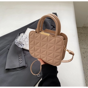 Dettaglio borsa a mano beige in pelle trapuntata con chiusura dorata e manici doppi