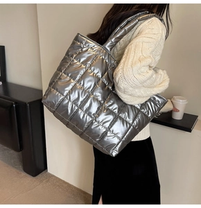 Close-up of a large silver metallic quilted tote bag carried by a model in a knit sweater