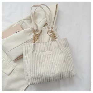 Detail of cream corduroy tote bag with fashion label and metal chain strap on beige blazer