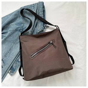 Flat lay of brown nylon tote bag with diagonal zipper pocket on denim jacket