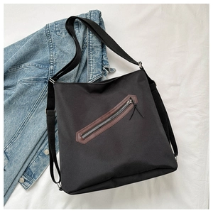 Detail of black canvas tote bag with diagonal zipper pocket and brown leather trim