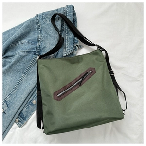 Close-up of a dark green canvas tote bag with diagonal zipper and leather trim detailing