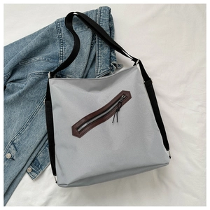 Detail of grey canvas tote bag featuring diagonal zip pocket with brown leather trim