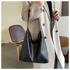 Detail of minimalist black hobo tote bag in soft leather shown on shoulder for daily commute