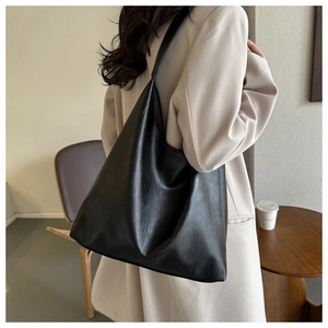 Detail of a large black tote bag with lychee texture worn by a model in a cafe