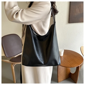 Black soft leather hobo tote bag shown worn by a model in a minimalist interior