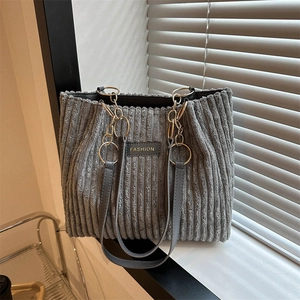 Grey corduroy tote bag with gold chain strap and fashion label on soft background