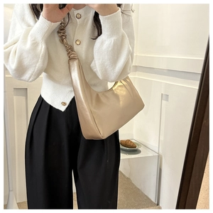 Detail of champagne gold underarm bag with pleated strap and metallic faux leather texture