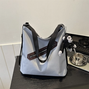 Large grey tote bag with diagonal zipper and plush monkey charm on a wooden desk