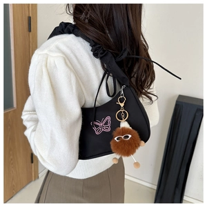 Détail du sac avec broderie papillon rose et pendentif en peluche sur l'épaule
