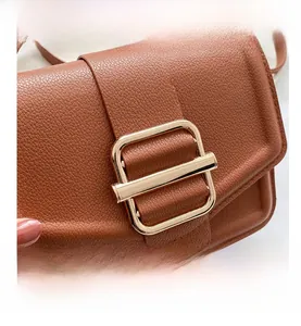 Close-up of brown litchi pattern leather crossbody bag with golden rectangular metal buckle