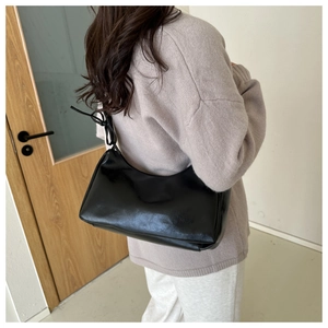 Close-up of a black glossy PU leather underarm bag with unique shoulder strap knot detail