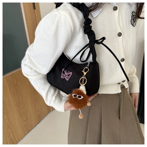 Détail d'un sac demi-lune noir avec broderie de papillon rose et bandoulière à volants