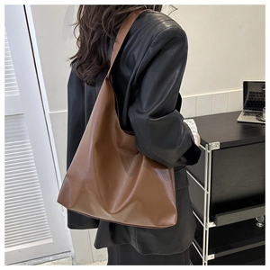 Close-up of a brown leather hobo bag worn over the shoulder on a black leather jacket