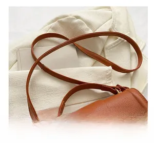 Detail of adjustable metal buckle and litchi texture on brown leather crossbody bag