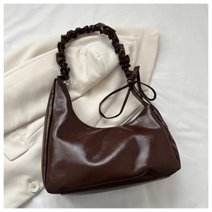 Detail of dark brown hobo bag with pleated shoulder strap and bow on beige blazer