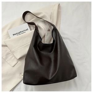 Detail of dark brown leather tote bag with wide strap on a cream blazer background