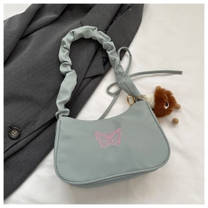 Détail du sac bandoulière vert clair avec broderie papillon rose et pendentif lion en peluche