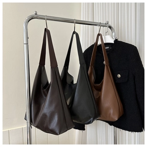 Three large Hobo tote bags in dark brown, black, and tan hanging on a minimalist rack