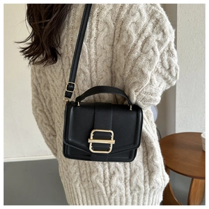 Close-up of black lychee texture handbag with gold buckle and beige sweater detail