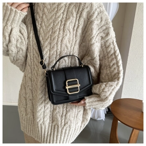 Detail of black pebbled leather crossbody bag with elegant gold rectangular metal buckle