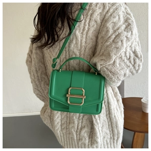 Detail view of green pebble leather bag with gold buckle on a beige sweater
