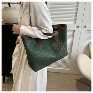 Detail of dark green woven tote bag with brown leather handles worn by a model